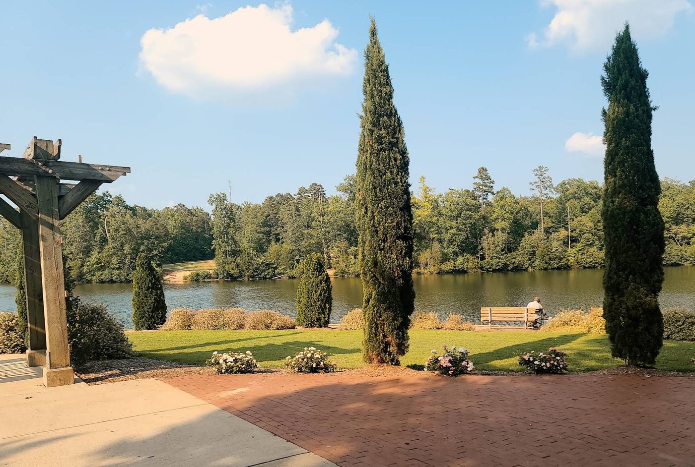 Red brick patio and lawn overlooking a lake, framed by tall evergreens